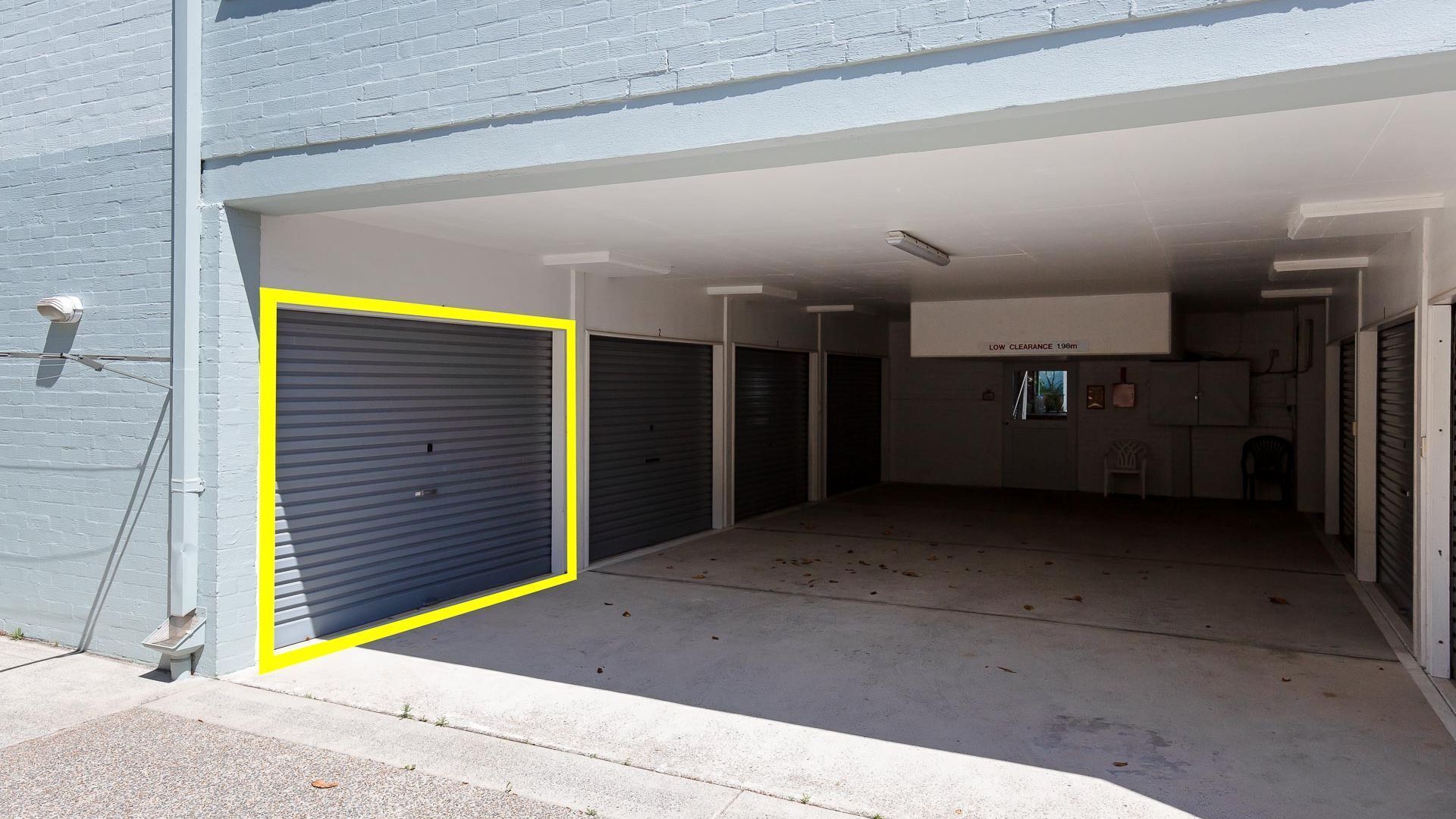 A parking garage with multiple closed garage doors, a low clearance sign, and a visible security camera.