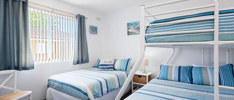 Een kamer met stapelbedden, een eenpersoonsbed, een stoel, een nachtkastje en een raam met gordijnen.