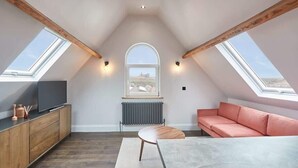 Un dormitorio tipo loft con tragaluces, televisor, sofá, mesa y radiador.