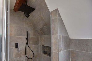 A shower area with a handheld showerhead, a wall-mounted control panel, and a shelf with toiletries.