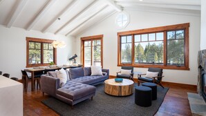 Amplia sala de estar con un sofá modular grande, una mesa de centro redonda y una chimenea. Varias ventanas ofrecen luz natural y vistas al exterior.