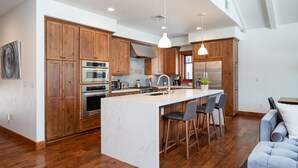 Una cocina amplia con armarios de madera, una isla grande con taburetes de bar, electrodomésticos de acero inoxidable e iluminación colgante.