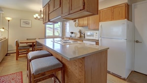 A kitchen with wooden cabinets, a white refrigerator, a microwave, and a dining area with a table and chairs. - Cc19 Chateau Claire 2 Bedroom Condo by RedAwning (Dillon)