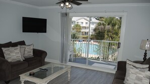 A living room with a glass coffee table, a brown sofa, and a TV mounted on the wall.