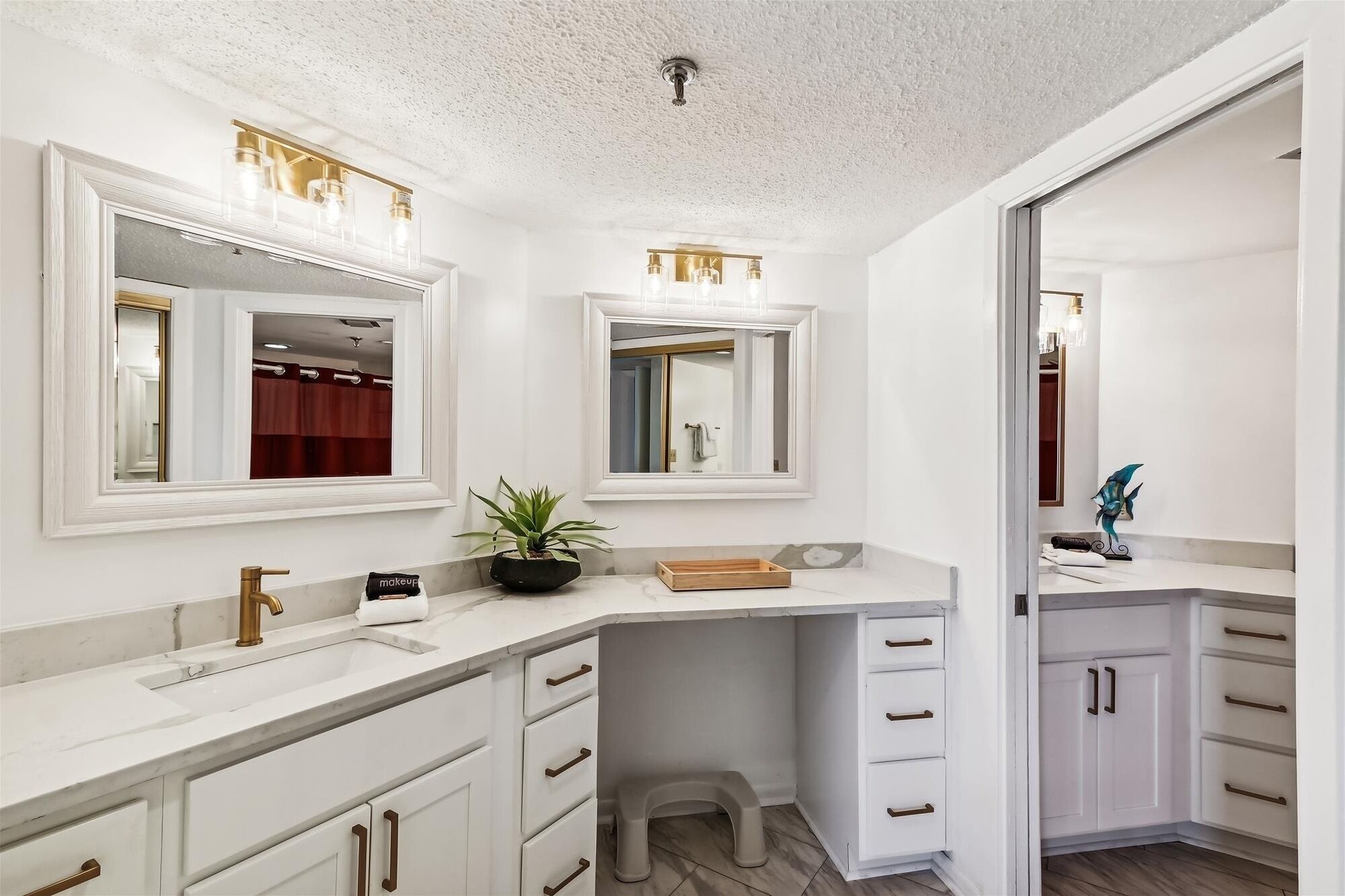 A modern bathroom with white cabinetry, a marble countertop, a sink with a gold faucet, and two wall-mounted mirrors with light fixtures.