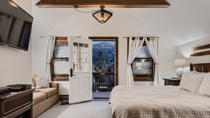 Een slaapkamer met een groot bed, een bank, een televisie en een balkon met uitzicht op bergen.