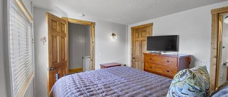A bedroom with a bed, a television on a wooden dresser, and a door leading to a hallway.