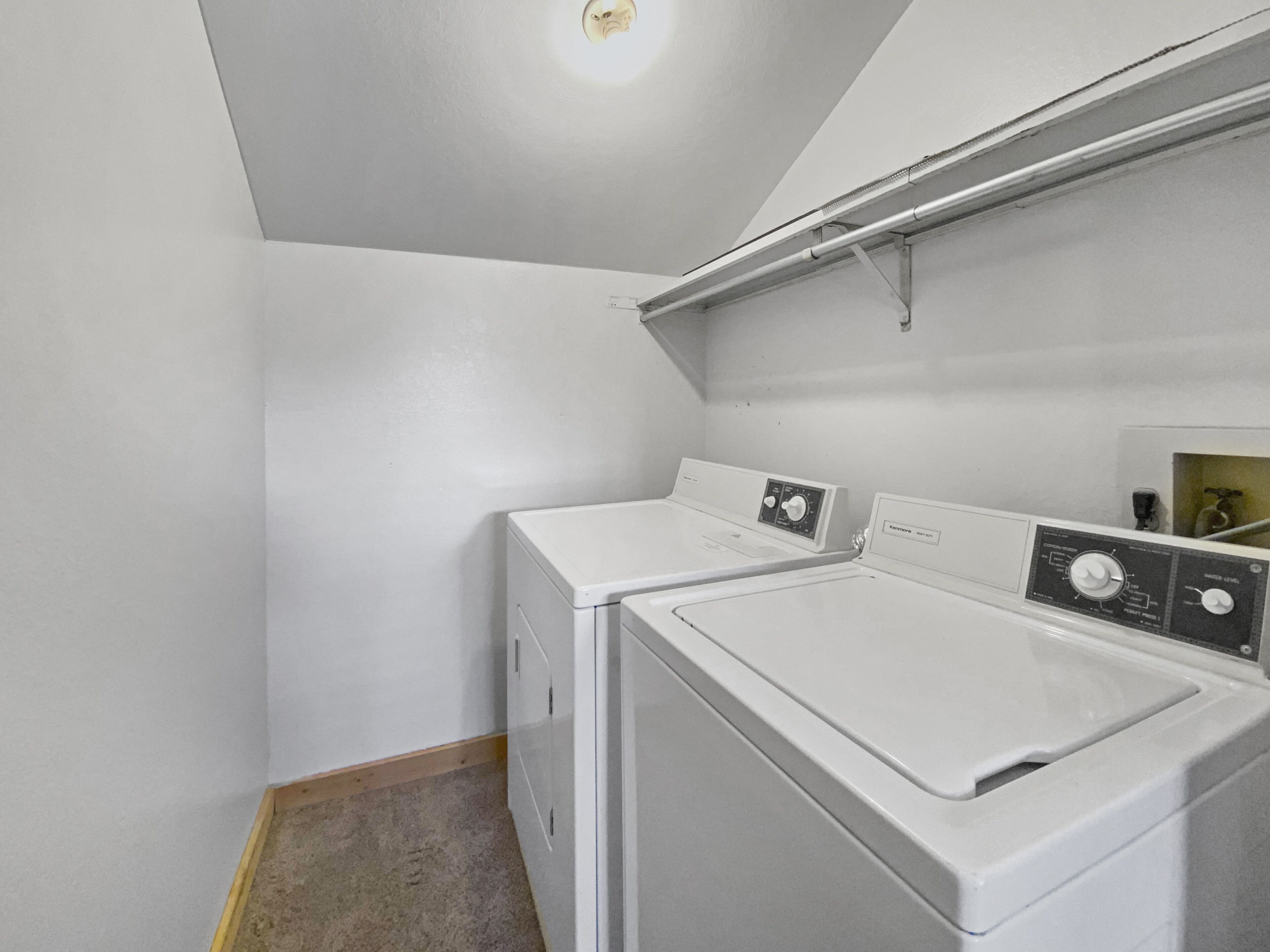 Ein Waschraum mit zwei weißen, frontbeladenen Waschmaschinen und Trocknern, einem Holzboden und einer schrägen Decke mit einer Leuchte.