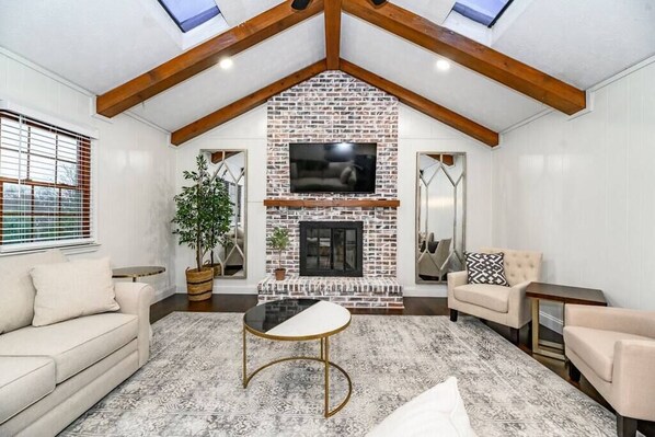 A living room with a brick fireplace, a sofa, a coffee table, and a TV mounted above the fireplace.