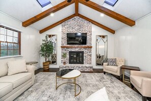Una sala de estar con chimenea de ladrillo, un sofá, una mesa de centro y un televisor sobre la chimenea.