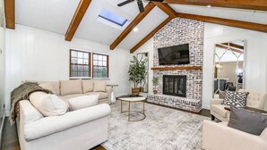 Un salon avec une cheminée en briques, un ventilateur de plafond et un grand téléviseur fixé au mur.