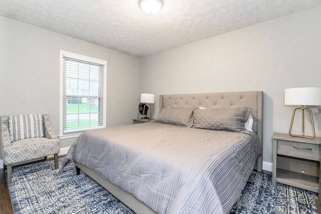 A bedroom with a large bed, a chair, a nightstand, and a lamp.