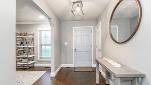 Un couloir avec un plancher en bois, une porte blanche, un miroir et un banc muni d’un plateau.