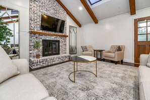 Una sala de estar con chimenea de ladrillo, televisor de pantalla plana, dos sillones y una alfombra estampada.