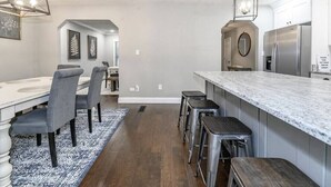 Une cuisine moderne dotée d’un plan de travail en marbre, d’appareils électroménagers en acier inoxydable et d’un coin repas avec des chaises grises et un tapis à motifs.