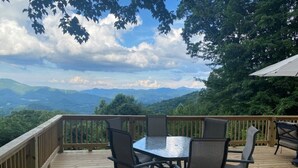 A wooden deck with a glass table and chairs, overlooking a mountainous landscape. - Ascendere - Amazing mountain views, 3 bedroom, 2 bath, central heat/AC, private. (Maggie Valley)