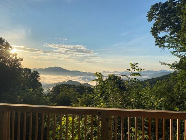 A view from a wooden deck overlooking a mountainous landscape with dense greenery and a clear sky.