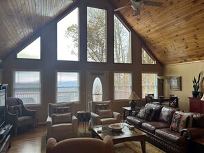 A spacious loft-style living room with high ceilings, large windows, and a view of the outdoors.