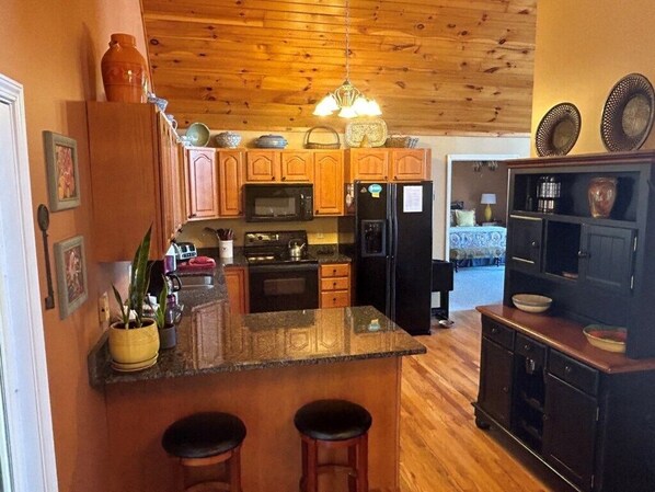 A kitchen with wooden cabinets, a microwave, a refrigerator, and a bar area with stools.
