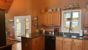 A kitchen with wooden cabinets, a black dishwasher, and a window with a view of trees. - Ascendere - Amazing mountain views, 3 bedroom, 2 bath, central heat/AC, private. (Maggie Valley)
