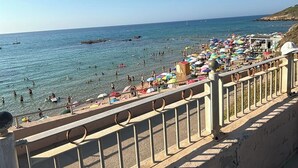 A beach with a stone railing, clear blue sky, and calm sea. - Residence L'Ancora (Castelsardo)