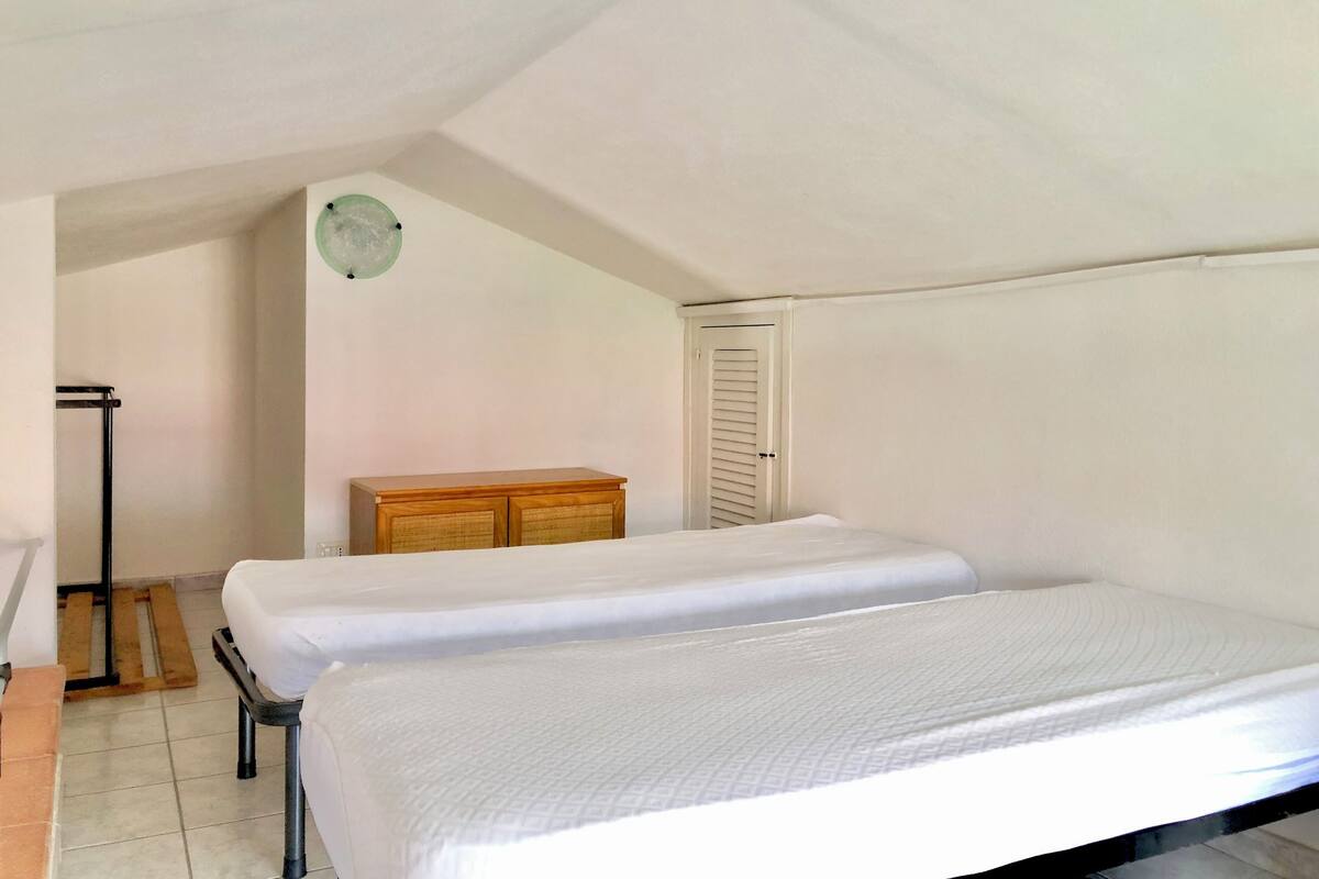 Ein kleines, schlichtes Zimmer mit zwei Einzelbetten, einer Holzkommode, einer Tür und einem Heizkörper.