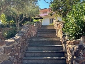 A stone staircase leading to a building with a red roof, surrounded by greenery. - Residence L'Ancora (Castelsardo)