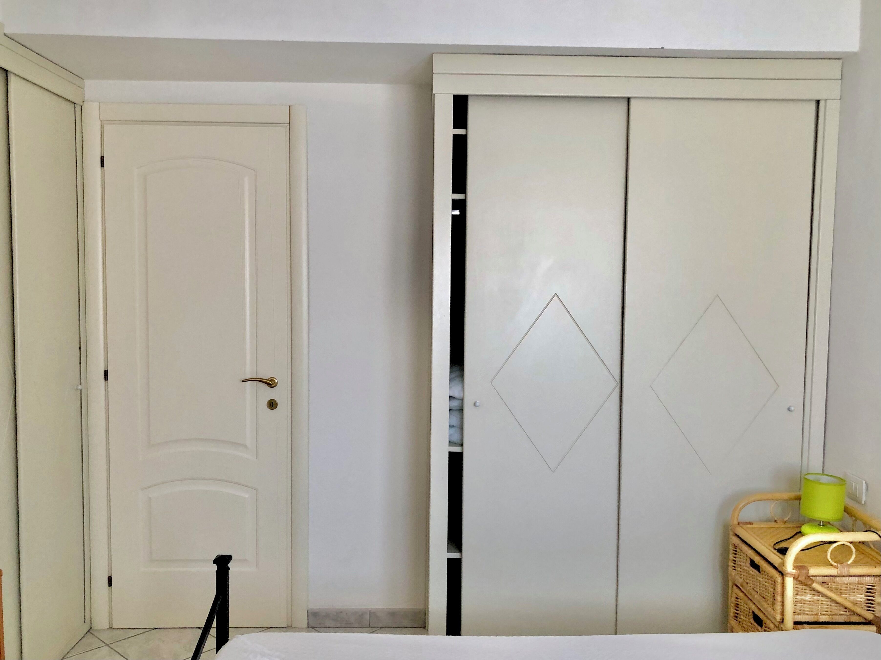 A room with a white door, a wardrobe with diamond-shaped cutouts, and a wicker basket with a green lamp.