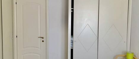 A room with a white door, a wardrobe with diamond-shaped cutouts, and a wicker basket with a green lamp.