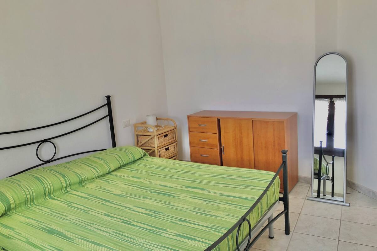 Ein Schlafzimmer mit einem Bett, einem Holzschrank, einem Korbwäscheschrank und einem Spiegel.