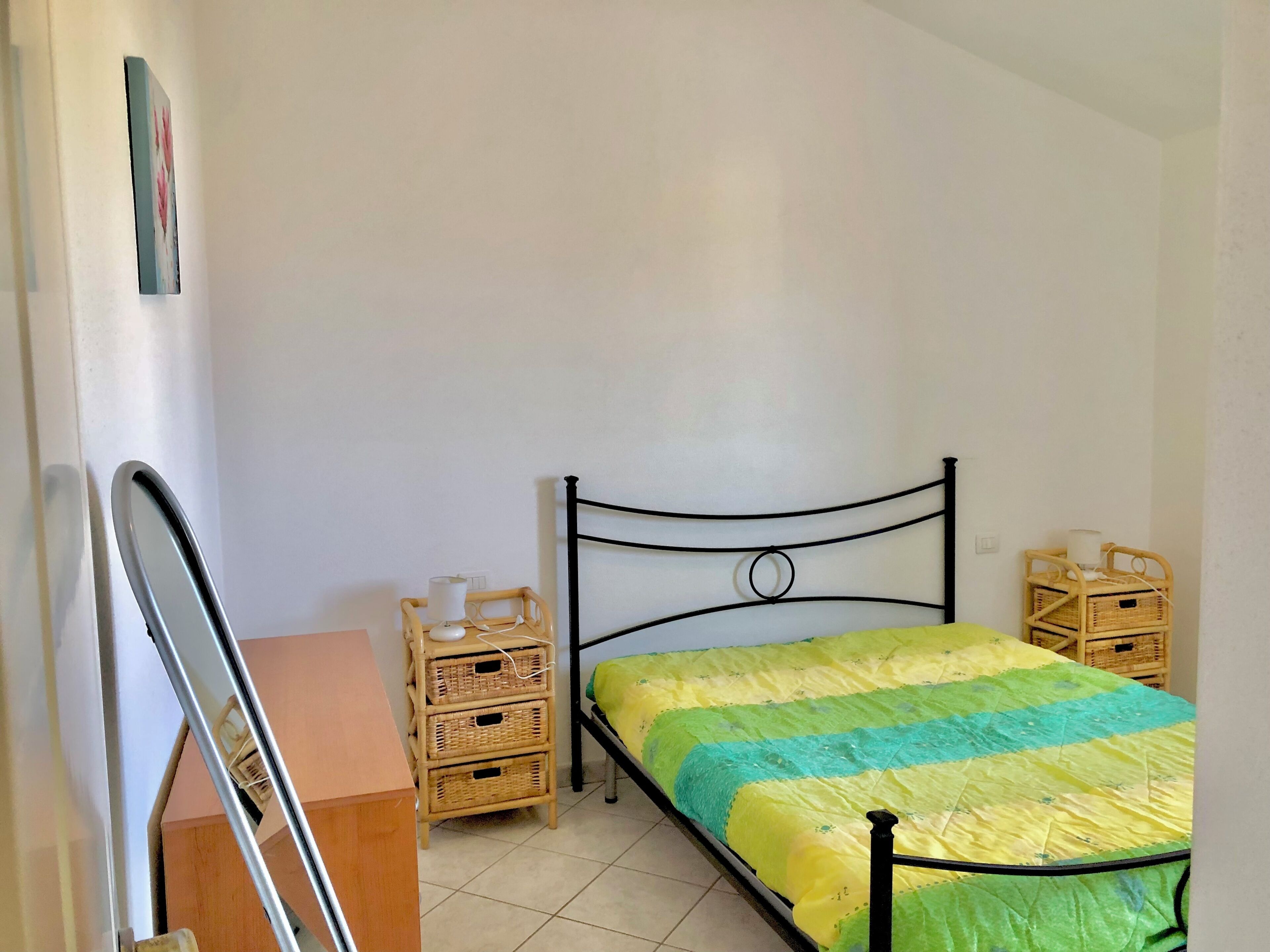 A bedroom with a bed, a bedside table, a lamp, and a wall-mounted shelf.