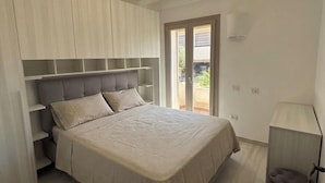 A bedroom with a bed, built-in shelving, a door to a balcony, and a bedside lamp. - Residence L'Ancora (Castelsardo)