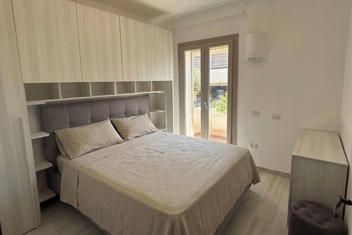 Ein Schlafzimmer mit Bett, Einbauschränken, einer Balkontür und einer Nachttischlampe.
