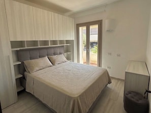 Ein Schlafzimmer mit Bett, Einbauschränken, einer Balkontür und einer Nachttischlampe.