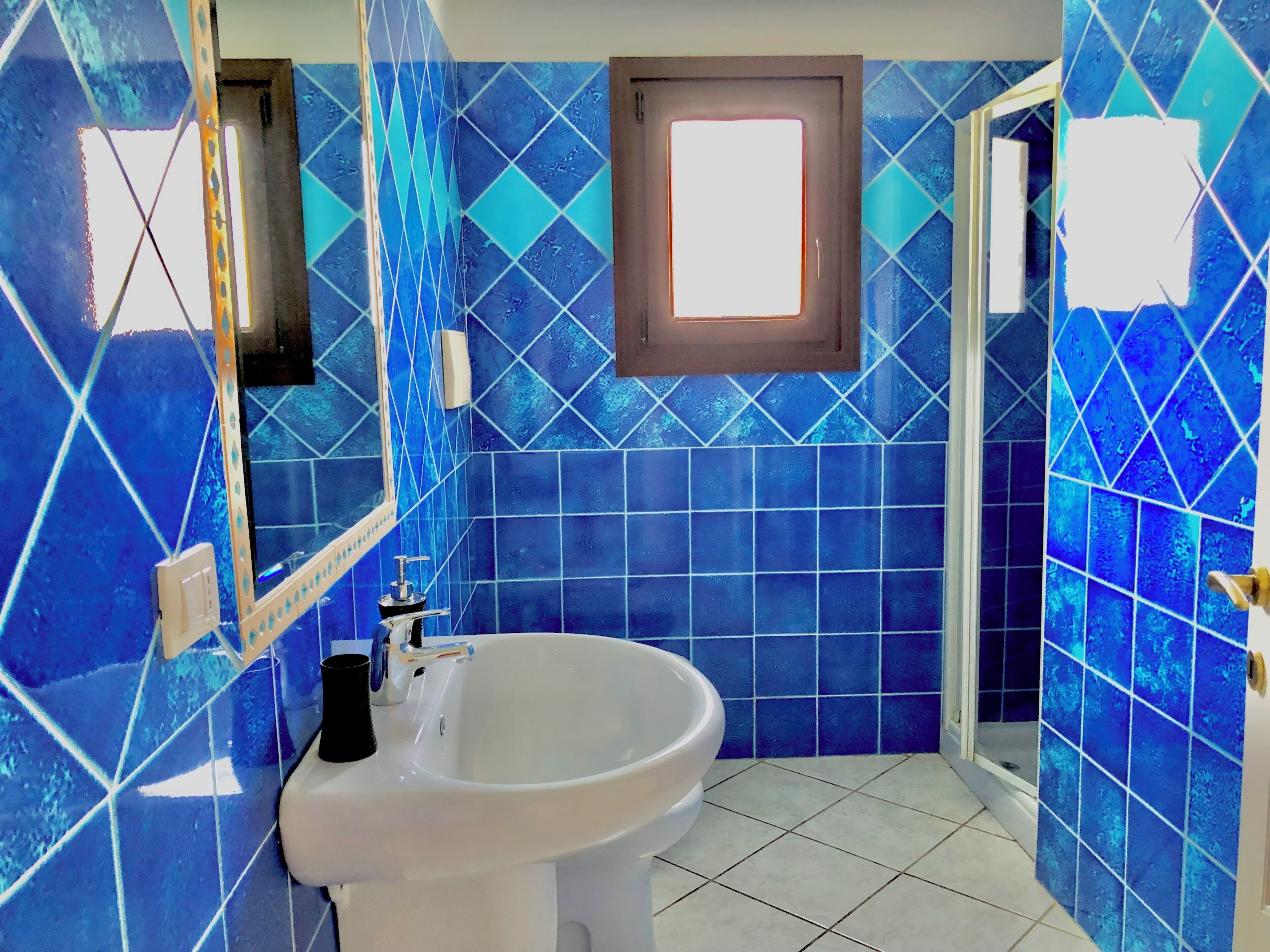 A bathroom with blue tiles, a white sink, and a mirror.