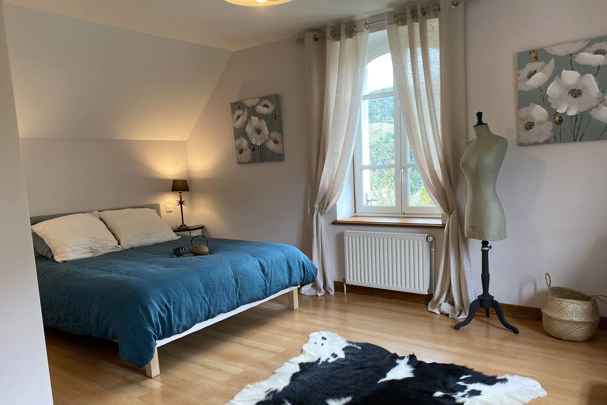Une chambre à coucher avec un lit, un mannequin, un radiateur, une fenêtre avec des rideaux et un tapis.