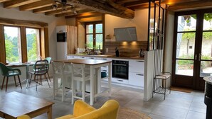 A modern kitchen with white cabinets, a built-in oven, and a dining area with a yellow chair and a round table. - Le Clos Saint Georges (Entraygues-sur-Truyere)