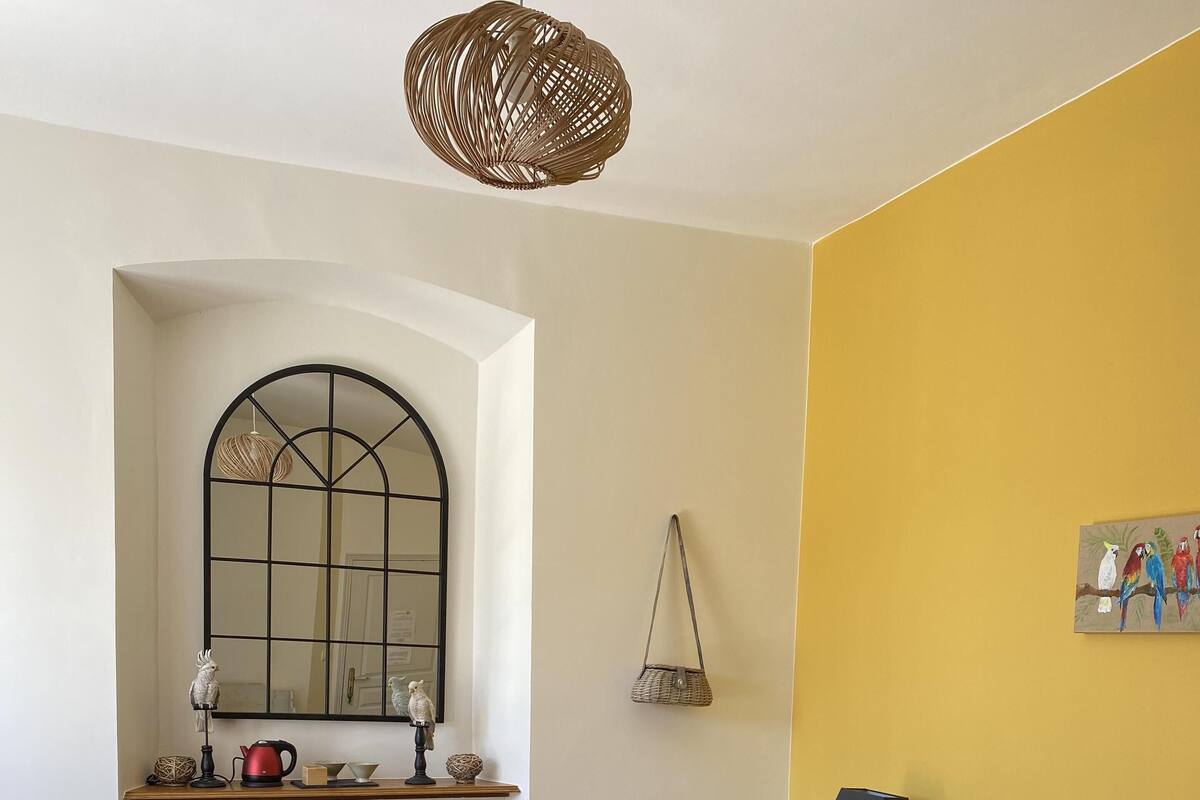Une chambre avec un grand lit, une fenêtre avec un miroir, un radiateur, une lampe et un tableau représentant des oiseaux accroché au mur.