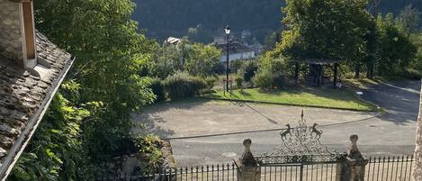 A view from a balcony overlooking a parking area, a stone building, and a mountainous landscape.