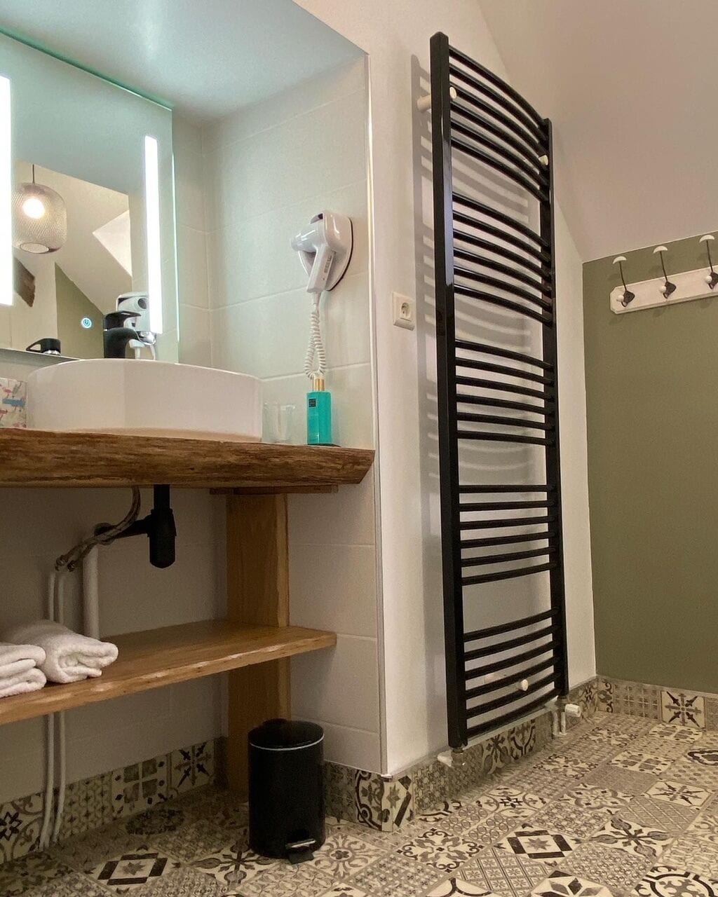 A bathroom with a wooden vanity, a black towel rack, and patterned floor tiles.
