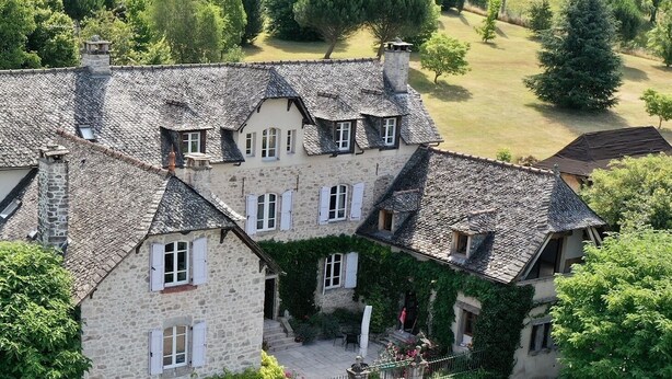 A stone building with multiple chimneys and windows, surrounded by greenery and a well-maintained lawn. - Le Clos Saint Georges (Entraygues-sur-Truyere)