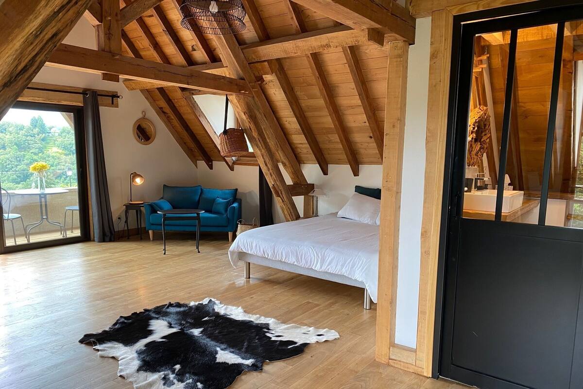 Une chambre avec un plafond en bois, un lit, un canapé bleu, une petite table et un tapis en peau de vache.