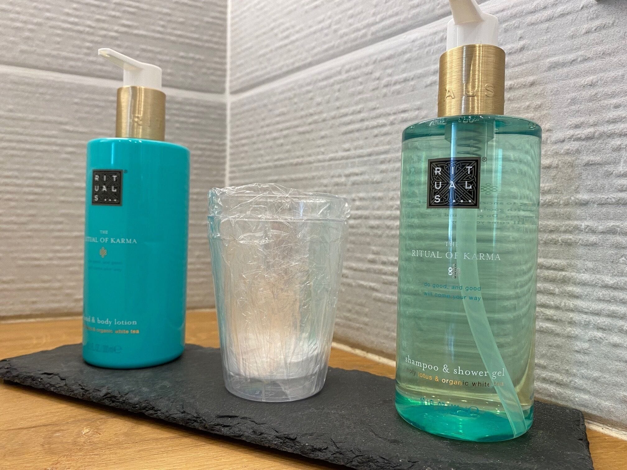 Dos botellas de loción corporal y champú de Rituals sobre una superficie de pizarra negra.