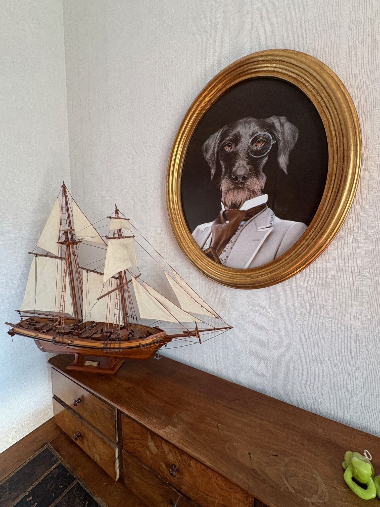 Un comò in legno con una nave modello e un ritratto incorniciato di un cane.
