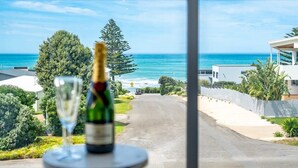 Vista sulla costa con una strada che conduce a un edificio, una bottiglia di champagne e un bicchiere su un tavolo.