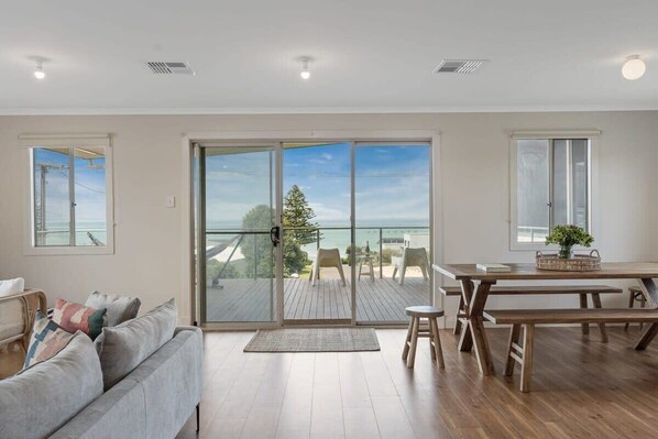A spacious living area with a sliding glass door leading to a balcony, a wooden dining table, and a sofa.