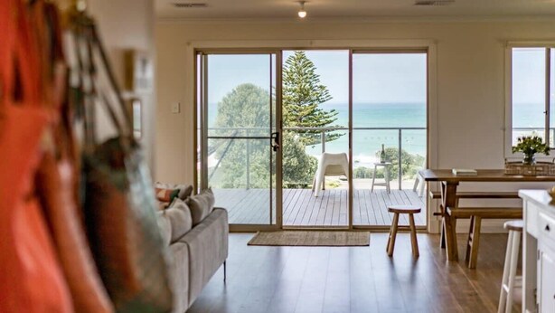Un soggiorno moderno con un'ampia porta finestra che dà su un balcone con vista sull'oceano.