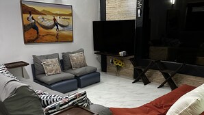 Un salon moderne avec un canapé gris, un canapé rouge, un téléviseur à écran plat et un tableau accroché au mur.