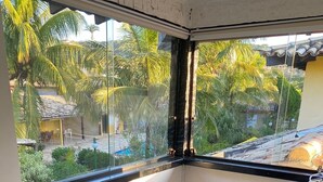 Un balcon avec vue sur les palmiers et une piscine, un canapé à carreaux bleus et blancs, et un fauteuil en cuir marron foncé.