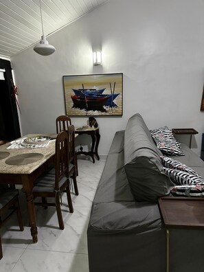 Un comedor con una mesa y sillas de madera, un sofá gris con almohadones estampados y un cuadro de barcos en la pared.
